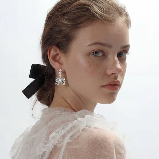 Perleøredobber med sløyfe i hvitt gullbelagt Eco- brass og zirkonia. Stiftene er laget av 925 sterlingsølv